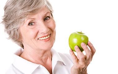 An elderly woman is holding a green apple in her hands.