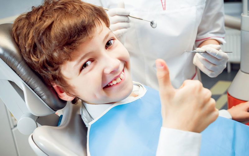 A young boy is giving a thumbs up while sitting in a dental chair.