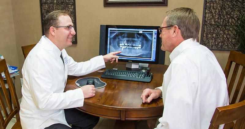 Two men are sitting at a table looking at a computer screen.