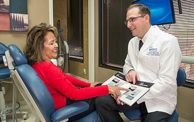 A dentist is talking to a patient in a dental chair.