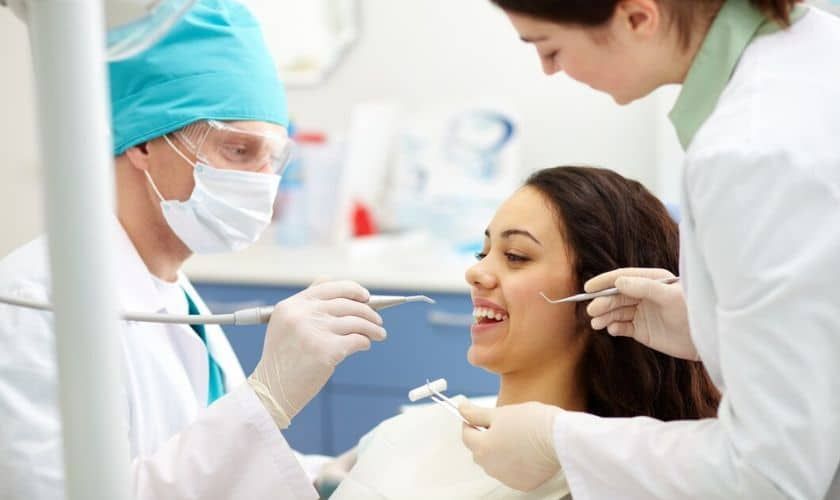 A woman is sitting in a dental chair while a dentist examines her teeth.