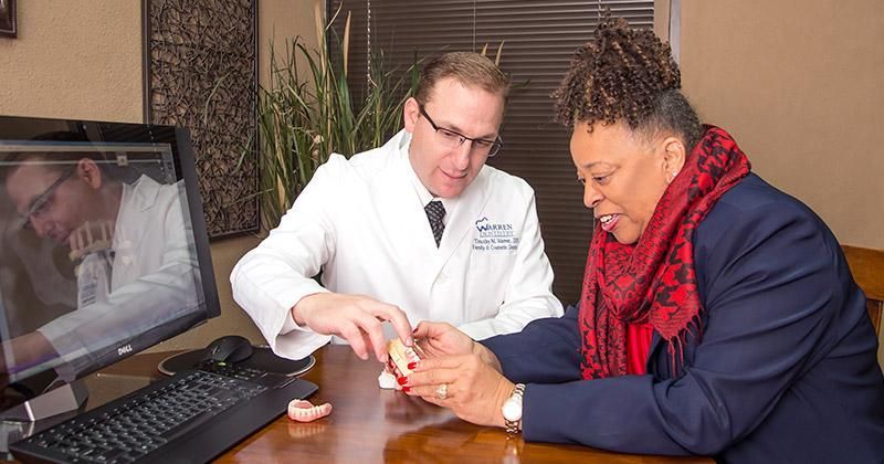 A man and a woman are sitting at a table looking at a model of teeth.