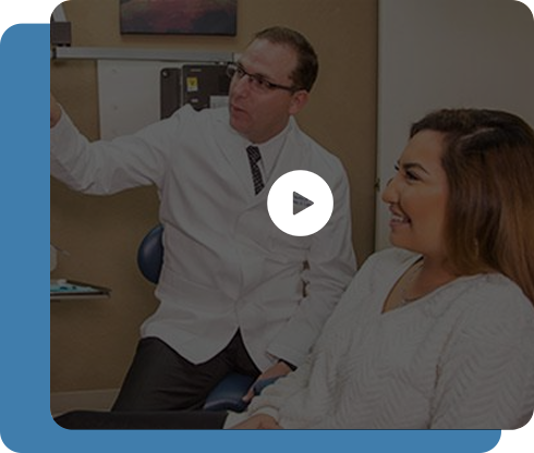 A man in a lab coat is talking to a woman in a dental chair.