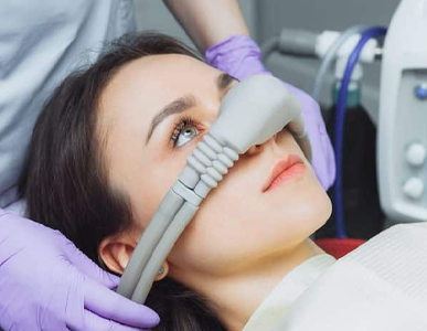 A woman is laying in a dental chair with an oxygen mask on her nose.