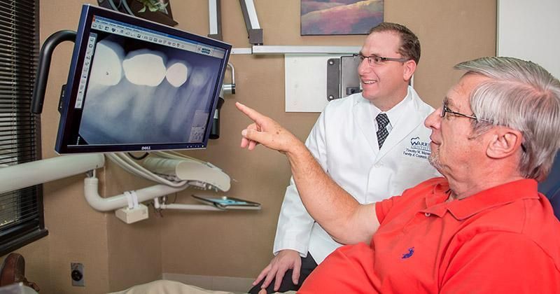 A man is sitting in a dental chair looking at an x-ray of his teeth.