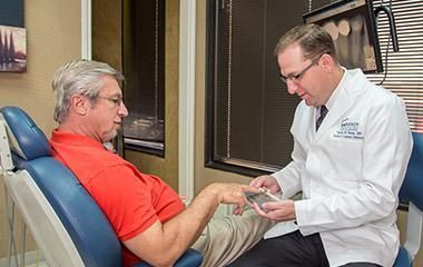 A man is sitting in a dental chair talking to a dentist.