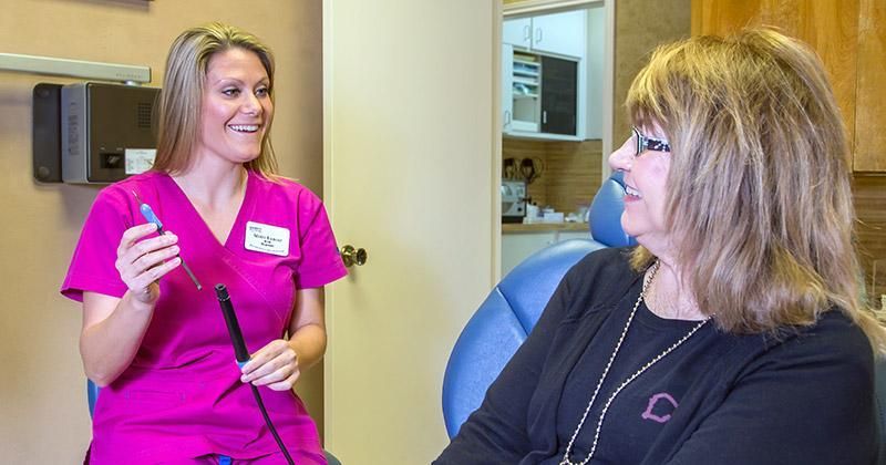 A woman is sitting in a dental chair talking to a nurse.