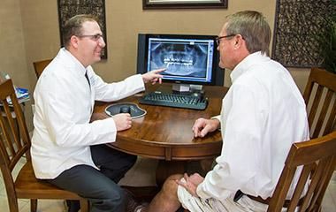 Two men are sitting at a table looking at a computer screen.