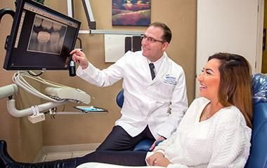 A woman is sitting in a dental chair while a dentist shows her an x-ray of her teeth.