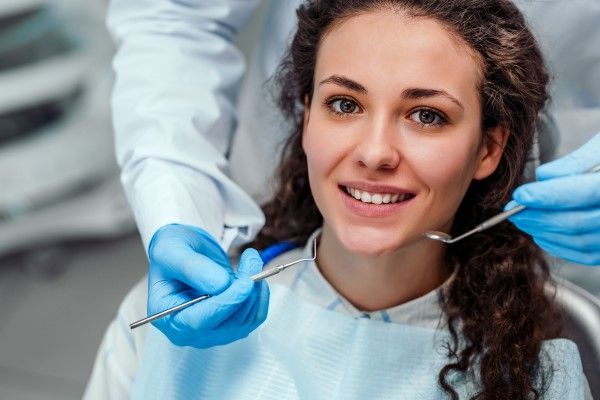 A woman is sitting in a dental chair while a dentist examines her teeth.