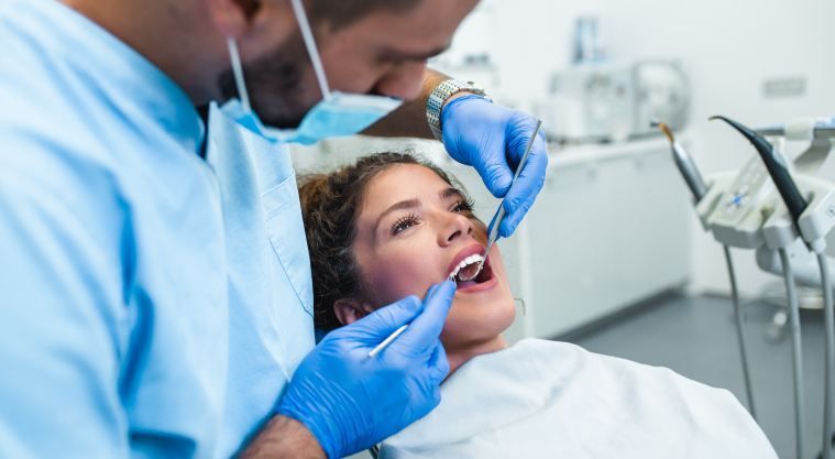 A dentist is examining a woman 's teeth in a dental office.