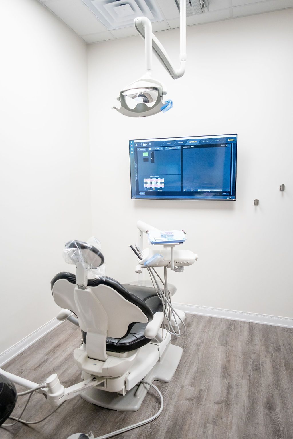 A dental office with a blue dental chair and a television on the wall.
