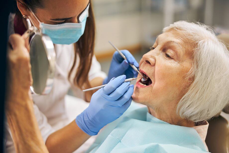 An elderly woman is having her teeth examined by a dentist.