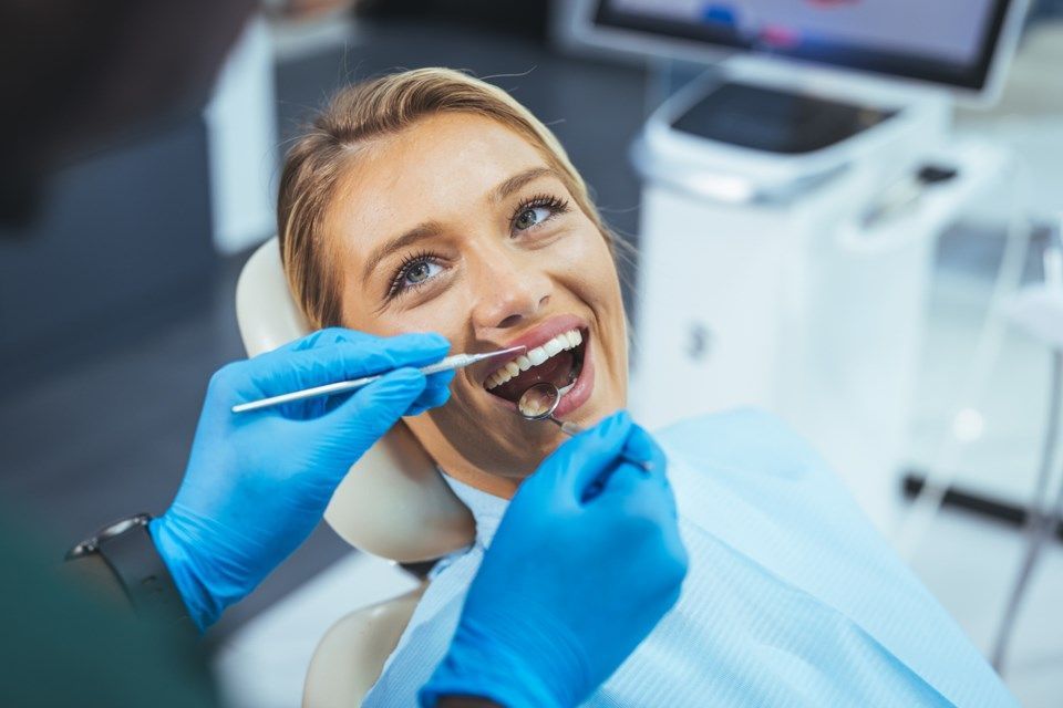 A woman is sitting in a dental chair while a dentist examines her teeth.