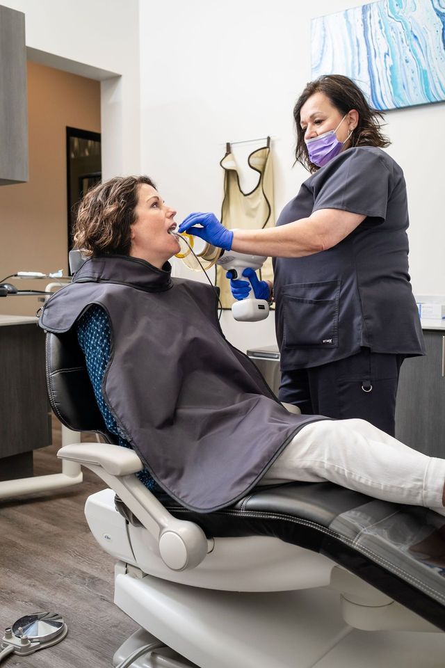 A woman in a pink shirt is talking to an older woman in a dental chair.