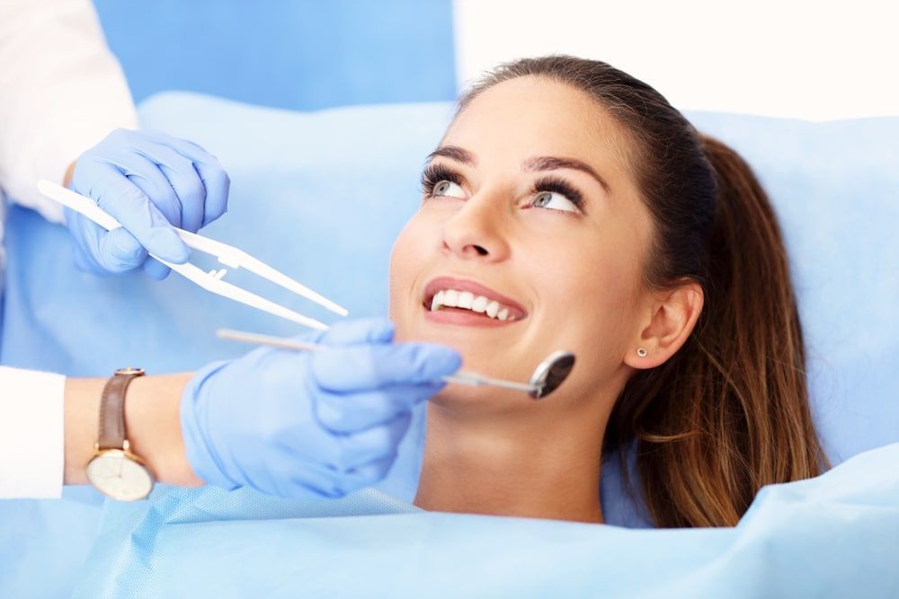 A woman is laying in a dental chair getting her teeth examined by a dentist.