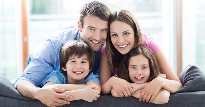 A family is laying on a couch and smiling for the camera.