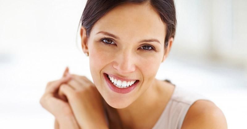 A close up of a woman smiling with her hand on her shoulder.