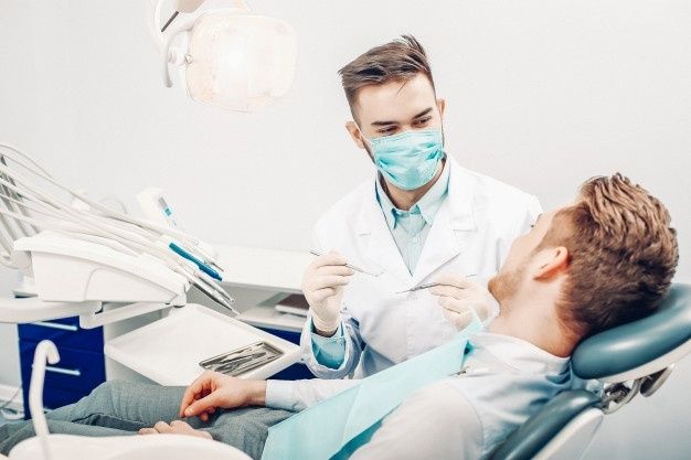 A man is sitting in a dental chair talking to a dentist.