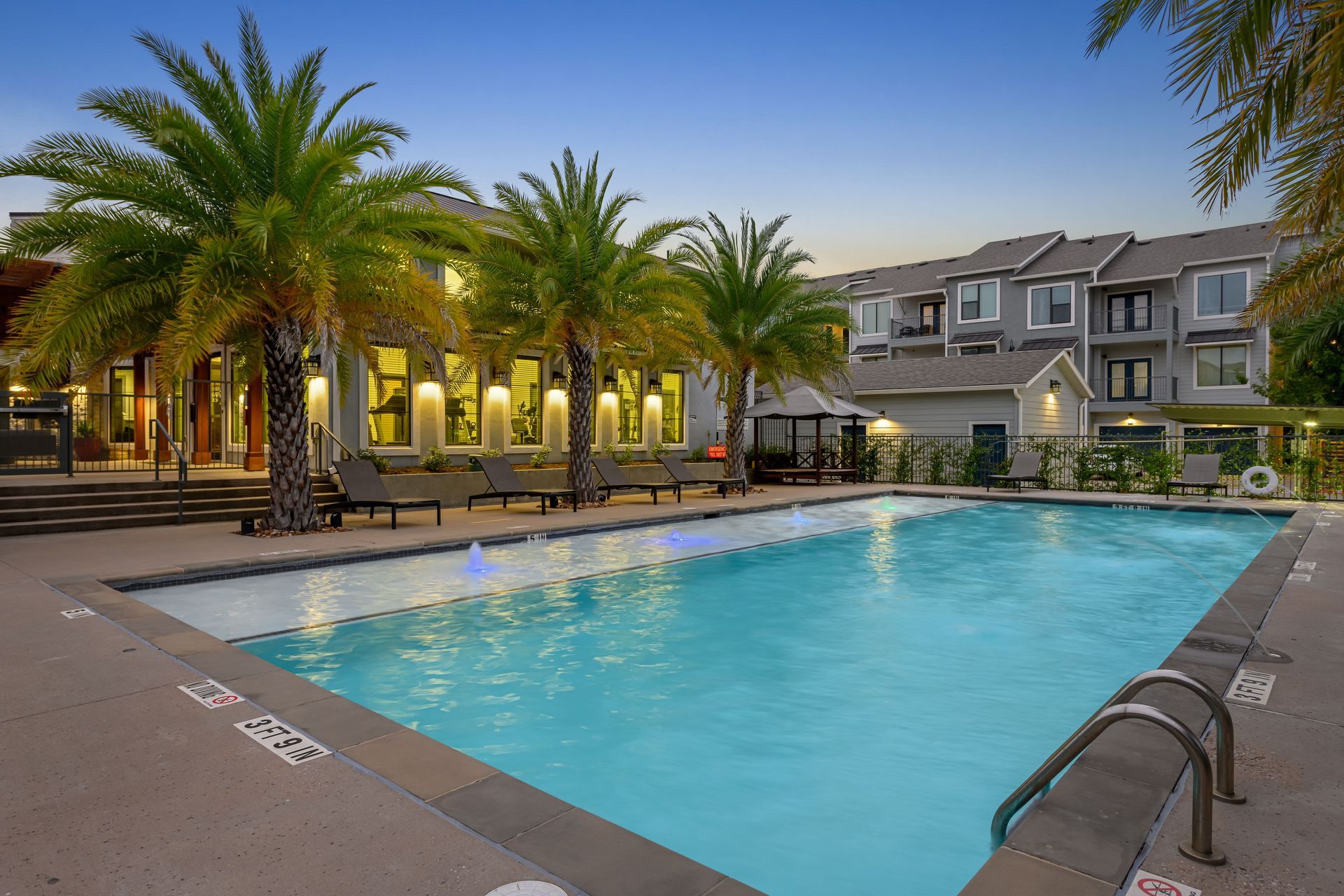 A large swimming pool surrounded by palm trees in front of a building at Marquis SoCo in South Austin, TX.