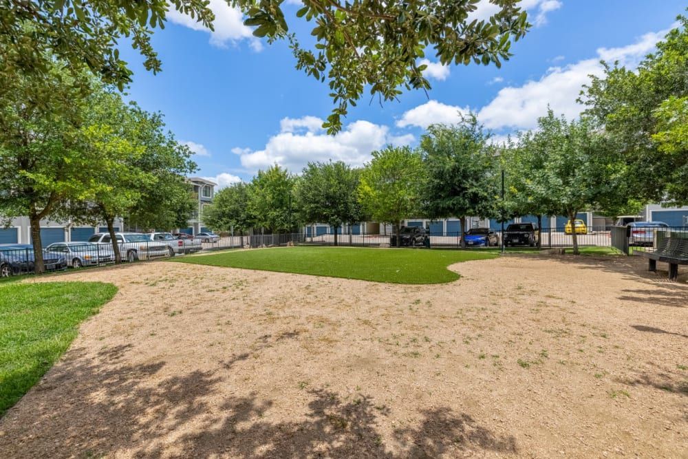A large grassy area with trees and cars parked in the background at Marquis SoCo in South Austin, TX.