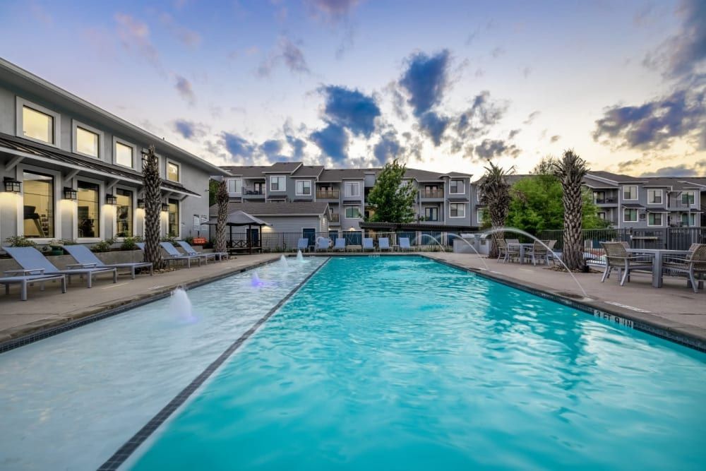 A large swimming pool surrounded by chairs and tables with a beautiful sky view at Marquis SoCo in South Austin, TX.