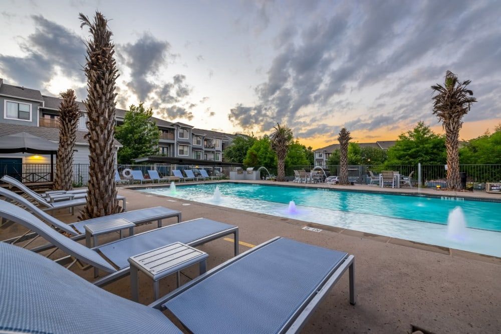 A resort-style swimming pool surrounded by lounge chairs and palm trees at Marquis SoCo in South Austin, TX.