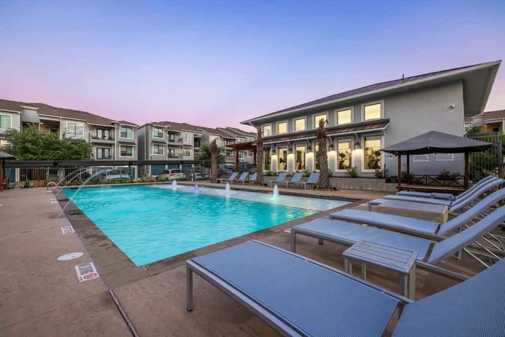 An apartment swimming pool surrounded by lounge chairs in front of apartment buildings at Marquis SoCo in South Austin, TX.