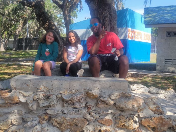 A man and two girls are sitting on a stone wall