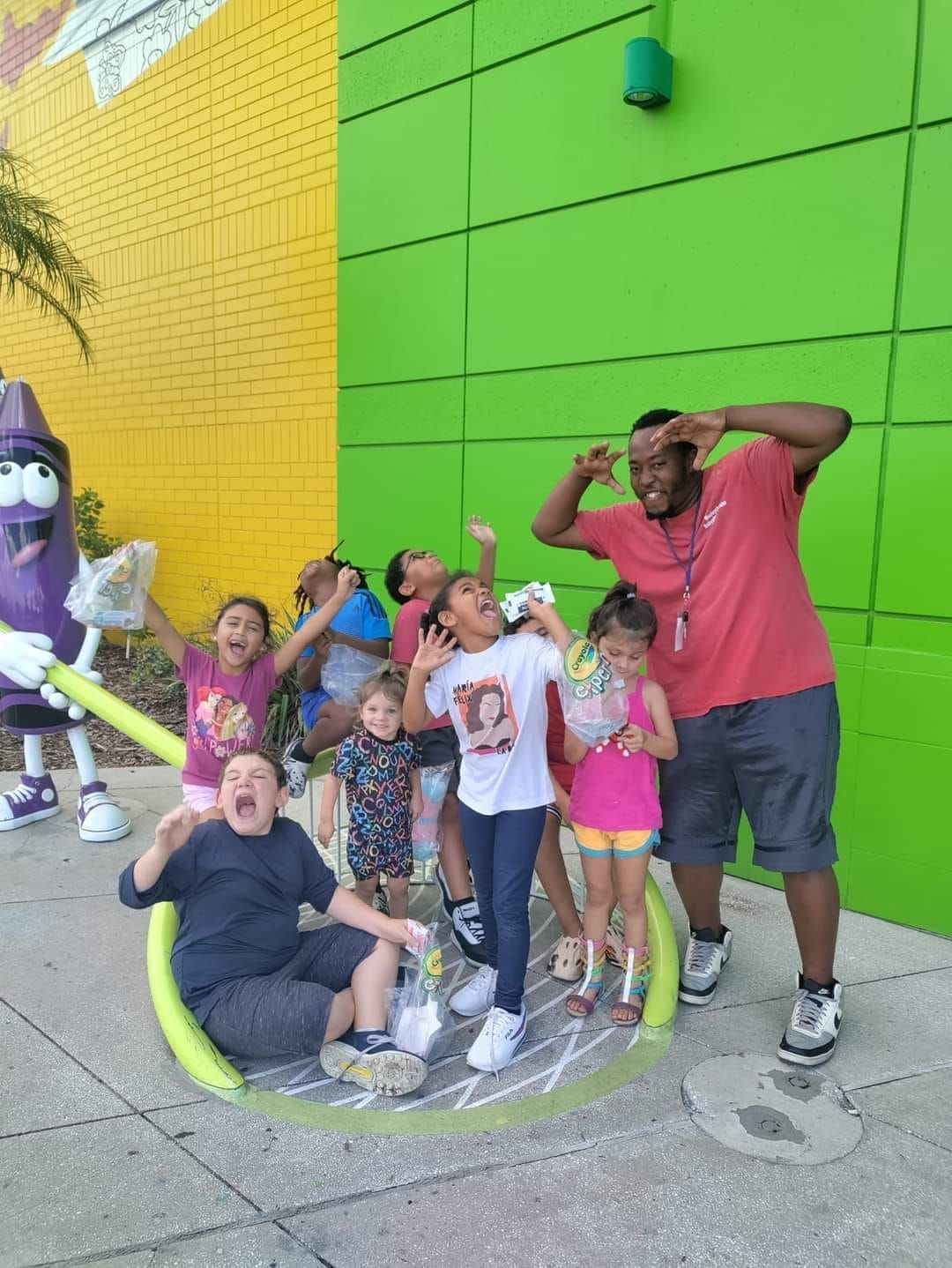 A group of children are posing for a picture in front of a green building.
