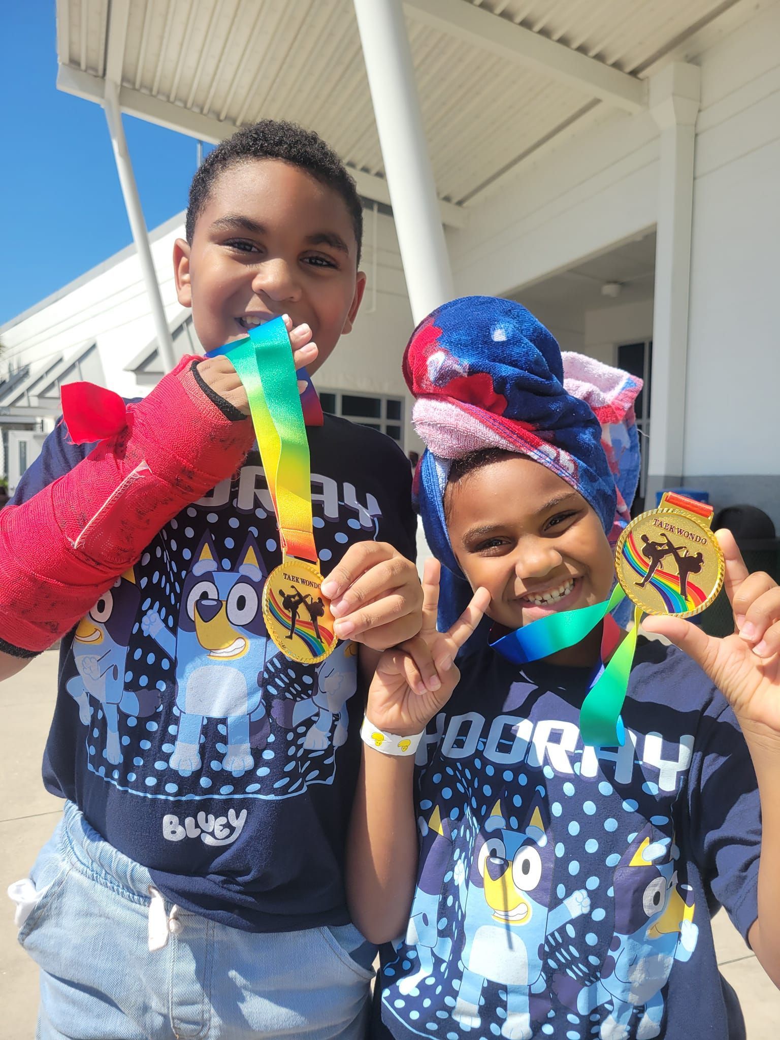A boy and a girl are holding medals in front of a building.
