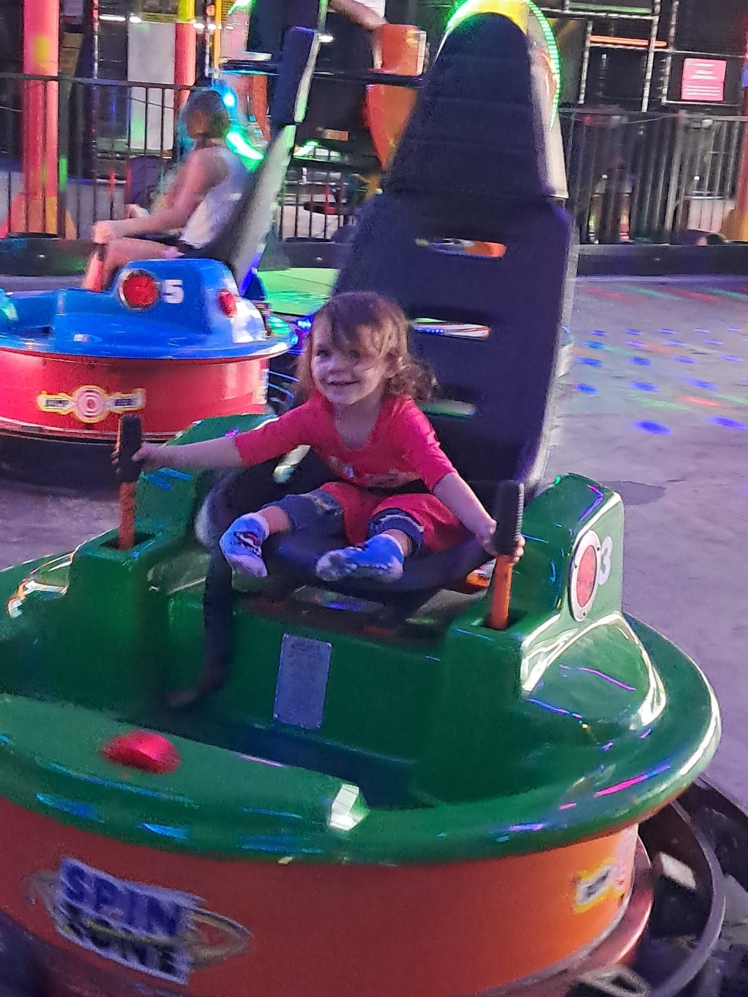 A little girl is sitting in a bumper car at an amusement park.