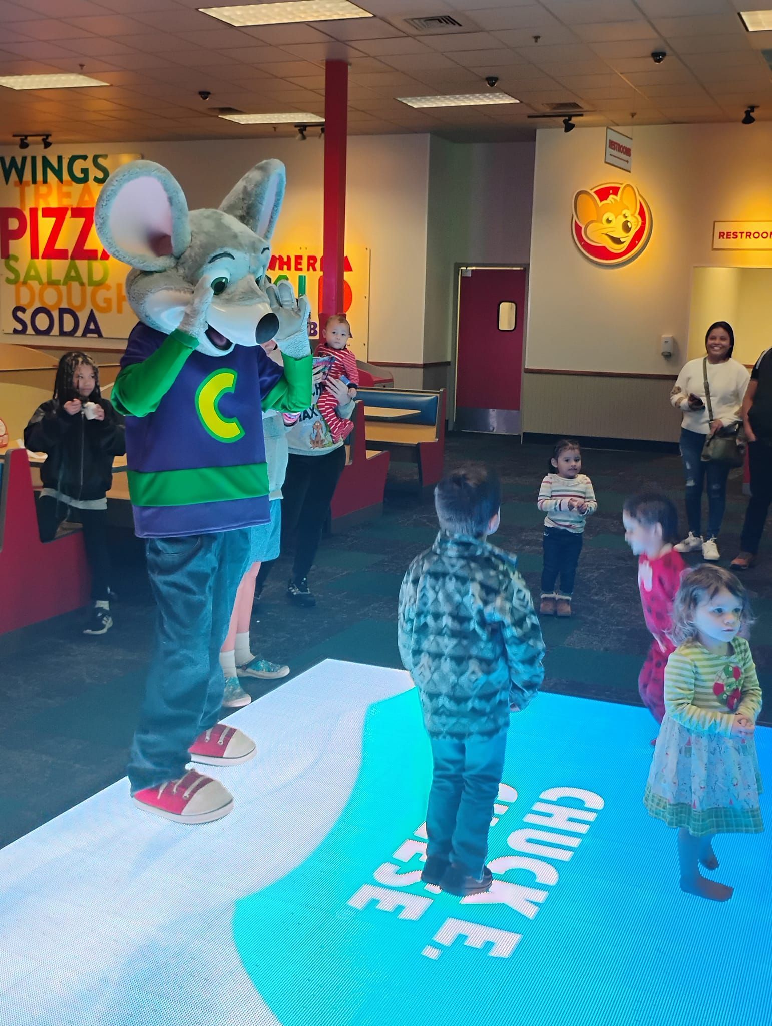A group of children are standing around a chuck e cheese mascot.