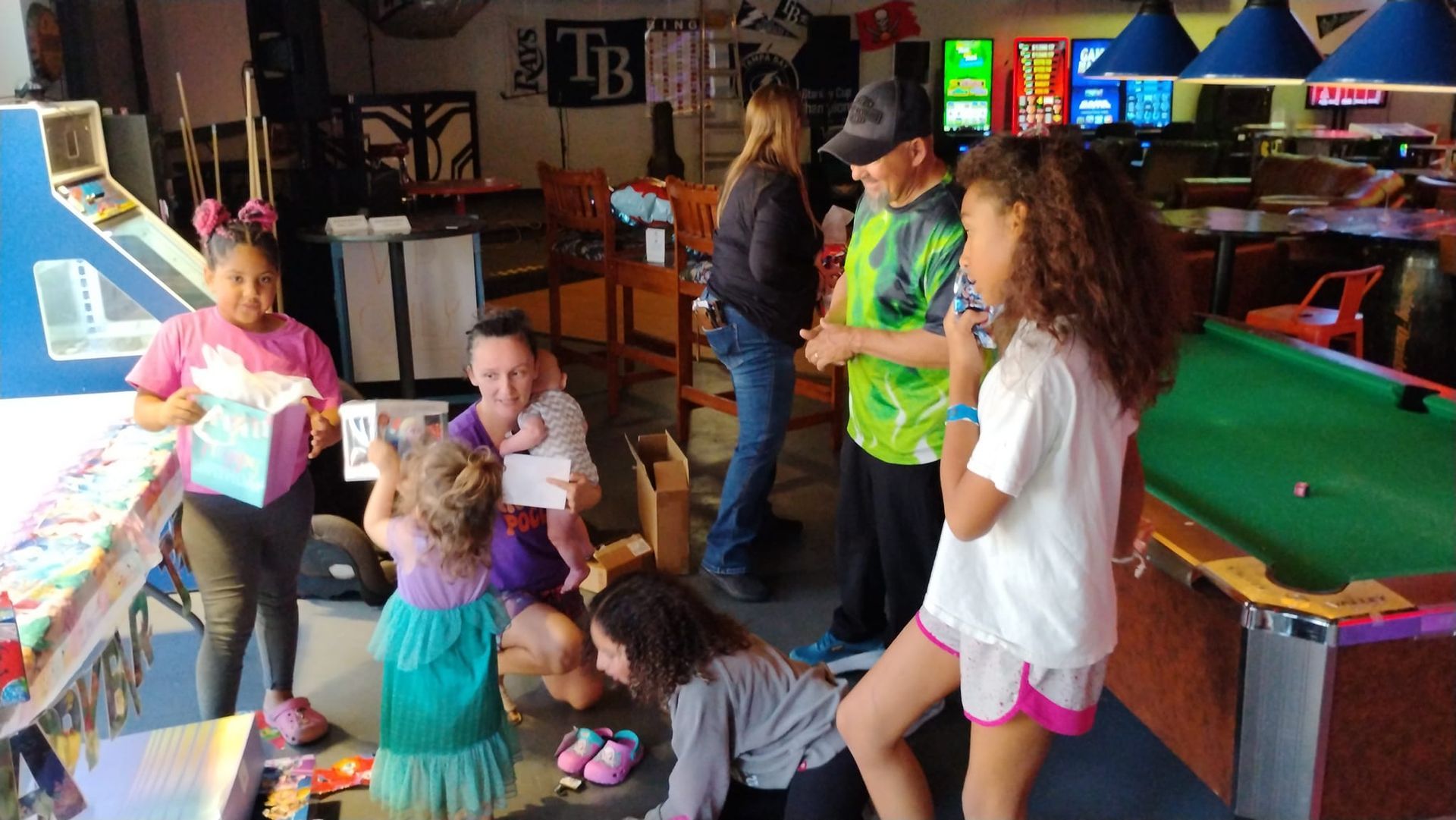 A group of children are standing around a pool table in an arcade.