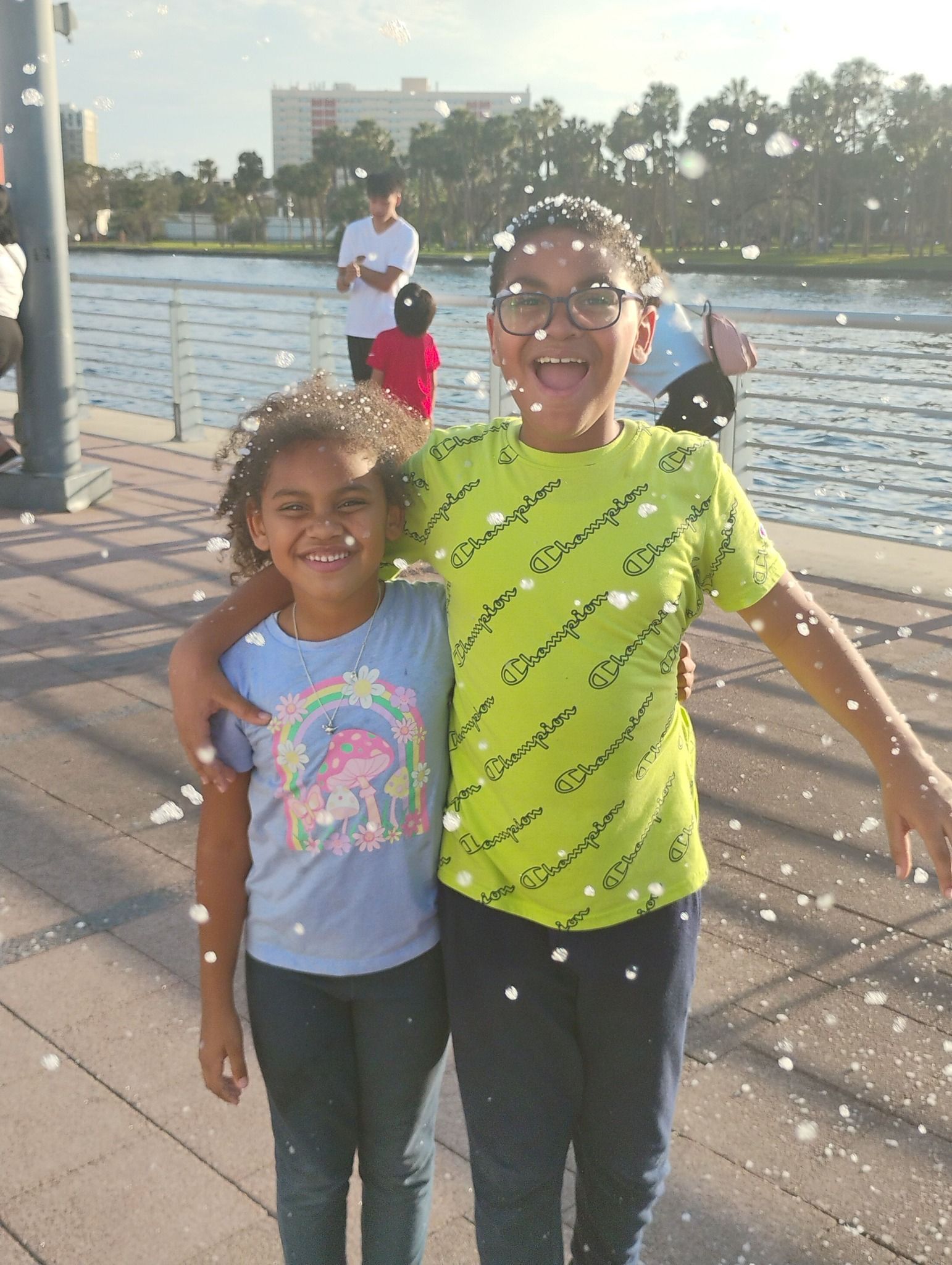 A boy and a girl are posing for a picture in front of a body of water