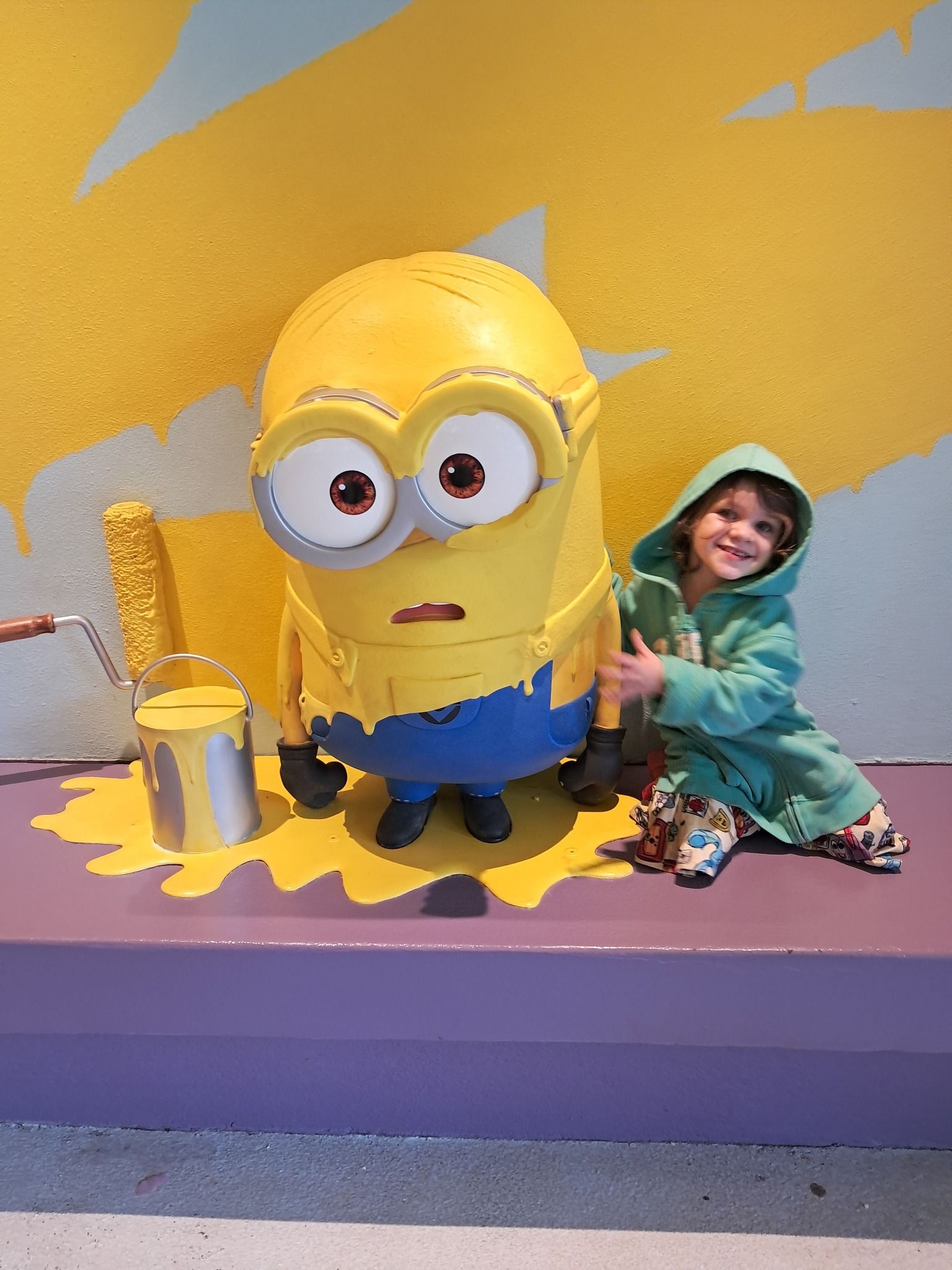 A little girl is sitting next to a statue of a minion.