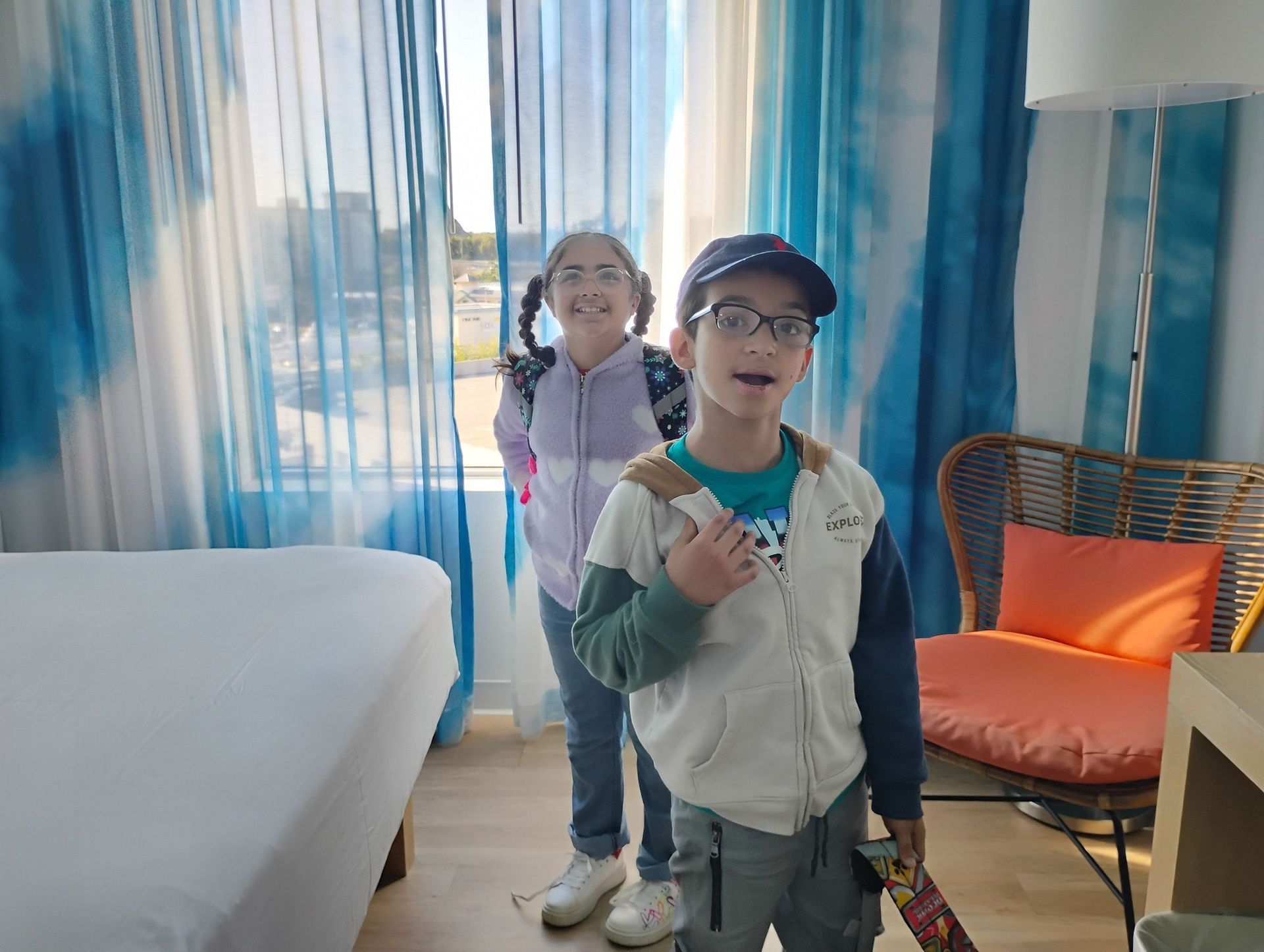 A boy and a girl are standing next to each other in a hotel room.