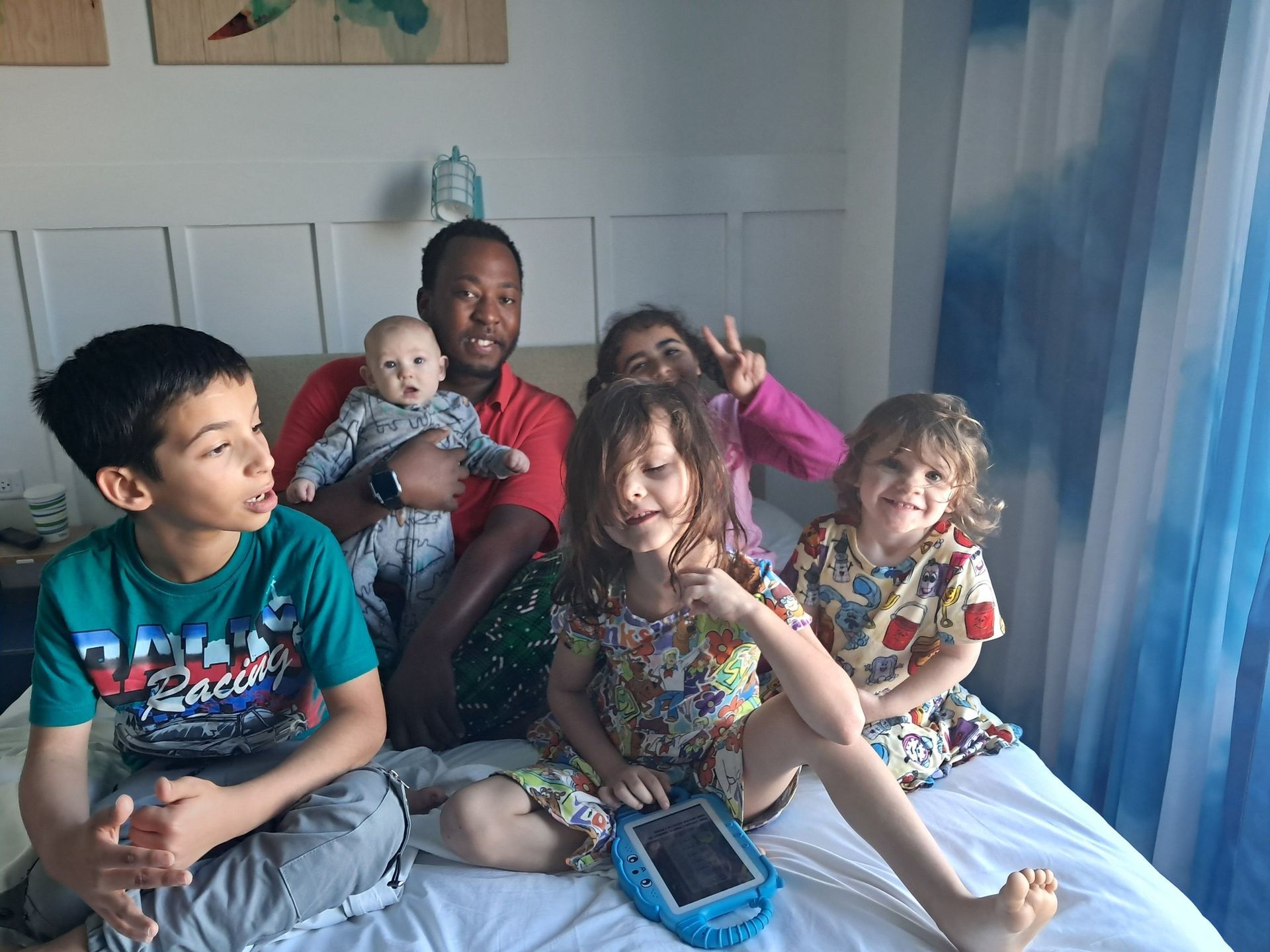 A group of children are sitting on a bed with a man holding a baby.