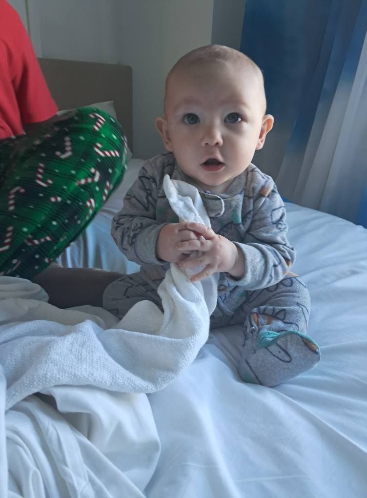 A baby is sitting on a bed holding a towel.