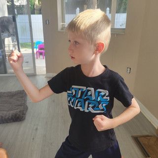 A young boy wearing a star wars t-shirt is standing in a living room.