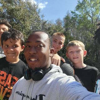 A man wearing headphones is taking a selfie with a group of young boys.