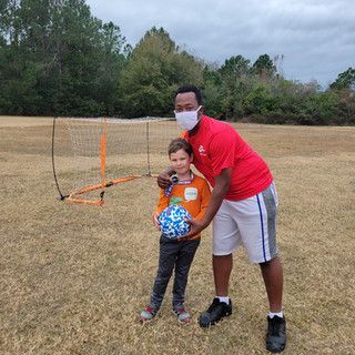 A man wearing a mask is standing next to a young boy holding a soccer ball.