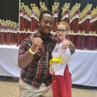 A man and a little girl are posing for a picture in front of trophies.
