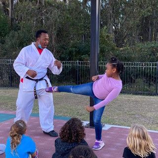 A man in a karate uniform is teaching a young girl how to kick a ball.