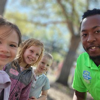 A man in a green shirt is standing next to two little girls and a boy.
