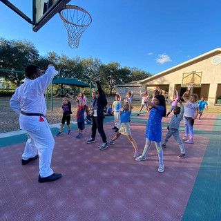 A man is playing basketball with a group of children on a court.