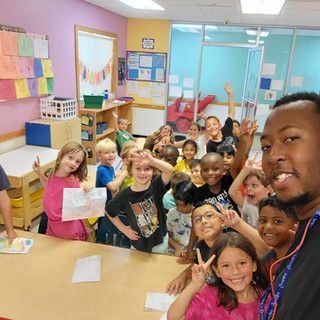 A man is taking a selfie with a group of children in a classroom.
