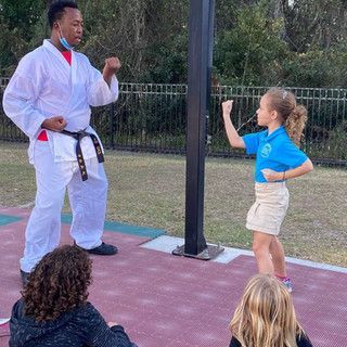 A man in a white karate uniform is teaching a young girl how to do karate.