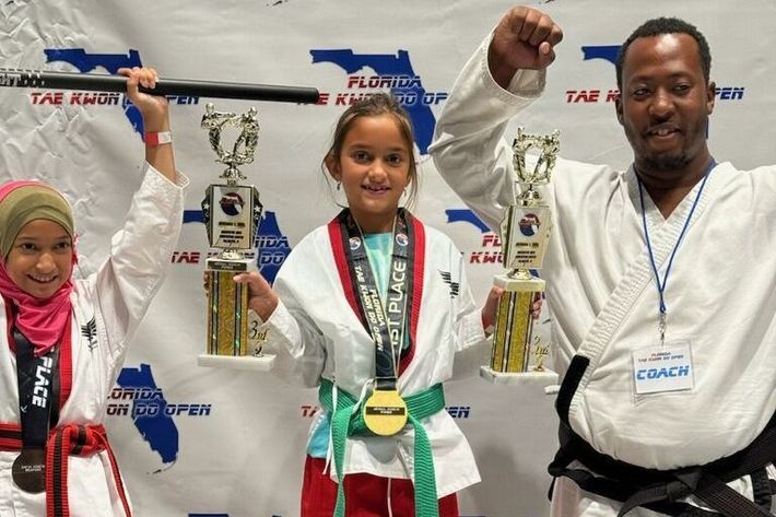 A man and two girls are standing next to each other holding trophies.