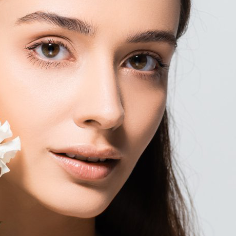Woman with fair skin and brown eyes, posing with a flower, looking towards the viewer.